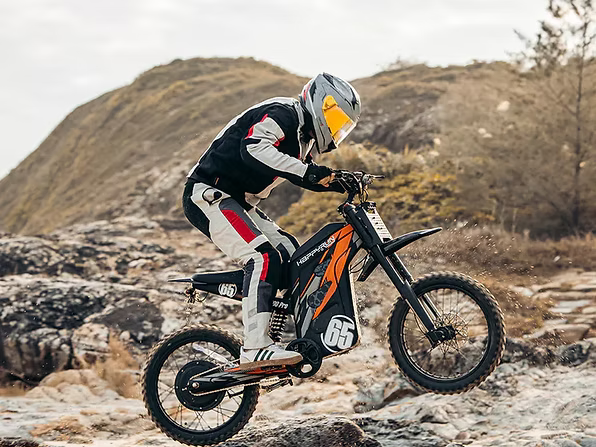 Person riding a dirt bike on rocky terrain with mountains in the background