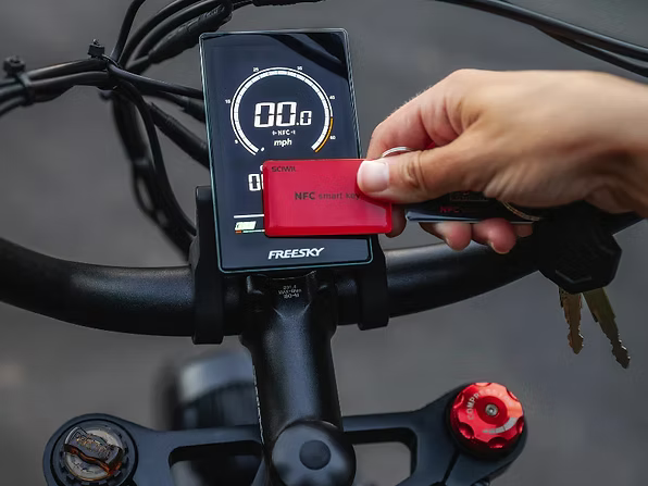 Person holding a red NFC smart card above a Freesky bike computer display.